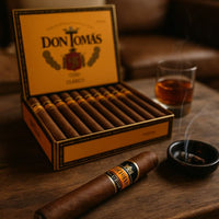 Box of Don Tomas cigars with a lit cigar and glass of whiskey on a wooden table. Vape Dokha UAE