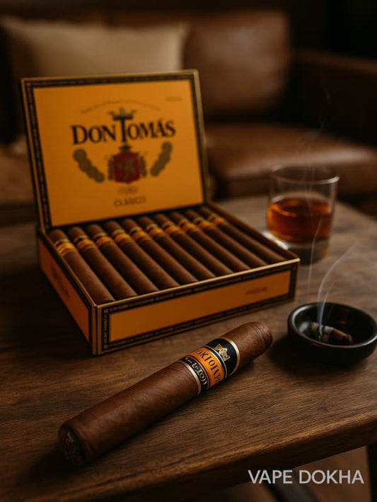 Box of Don Tomas cigars with a lit cigar and glass of whiskey on a wooden table. Vape Dokha UAE