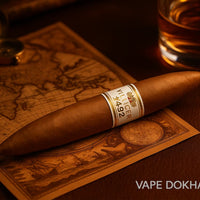 Cigar with a label on a world map, next to a glass of liquid, on a wooden surface.Vape Dokha UAE