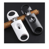 Two cigar cutters, one white and one black, on a black background with cigars. vape dokah UAE