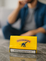 Yellow Old Holborn cigarette pack on a table with a blurred person in the background | Vape dokha UAE